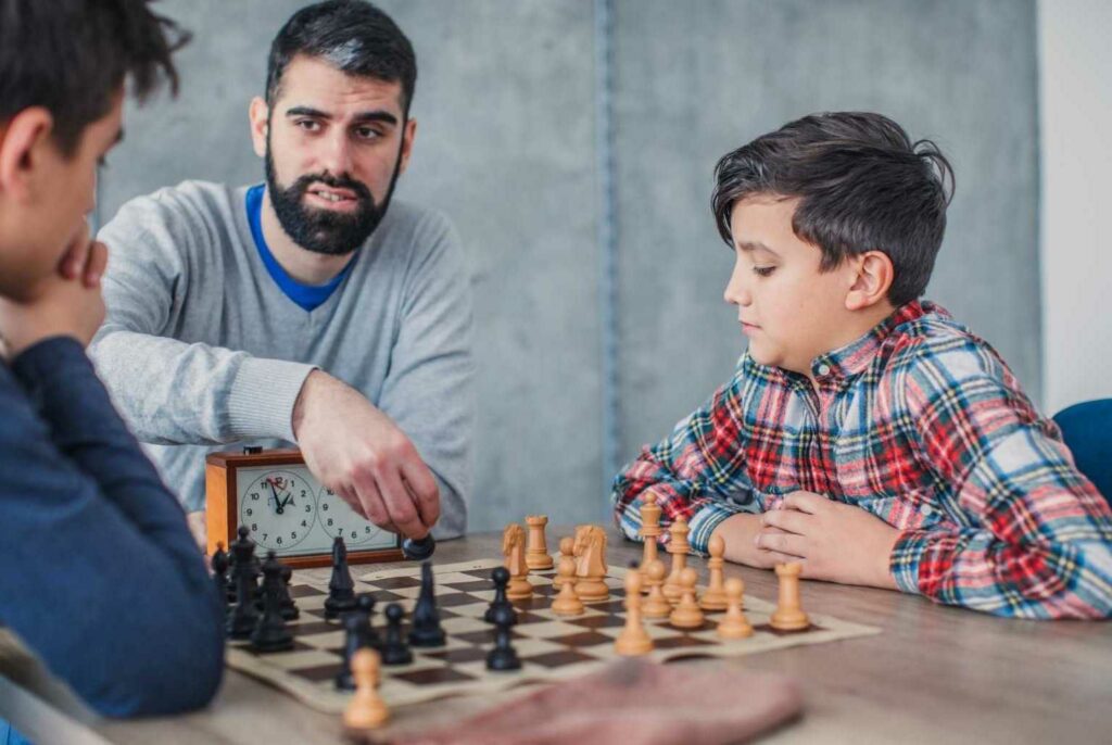 A man teaching 2 children to play chess